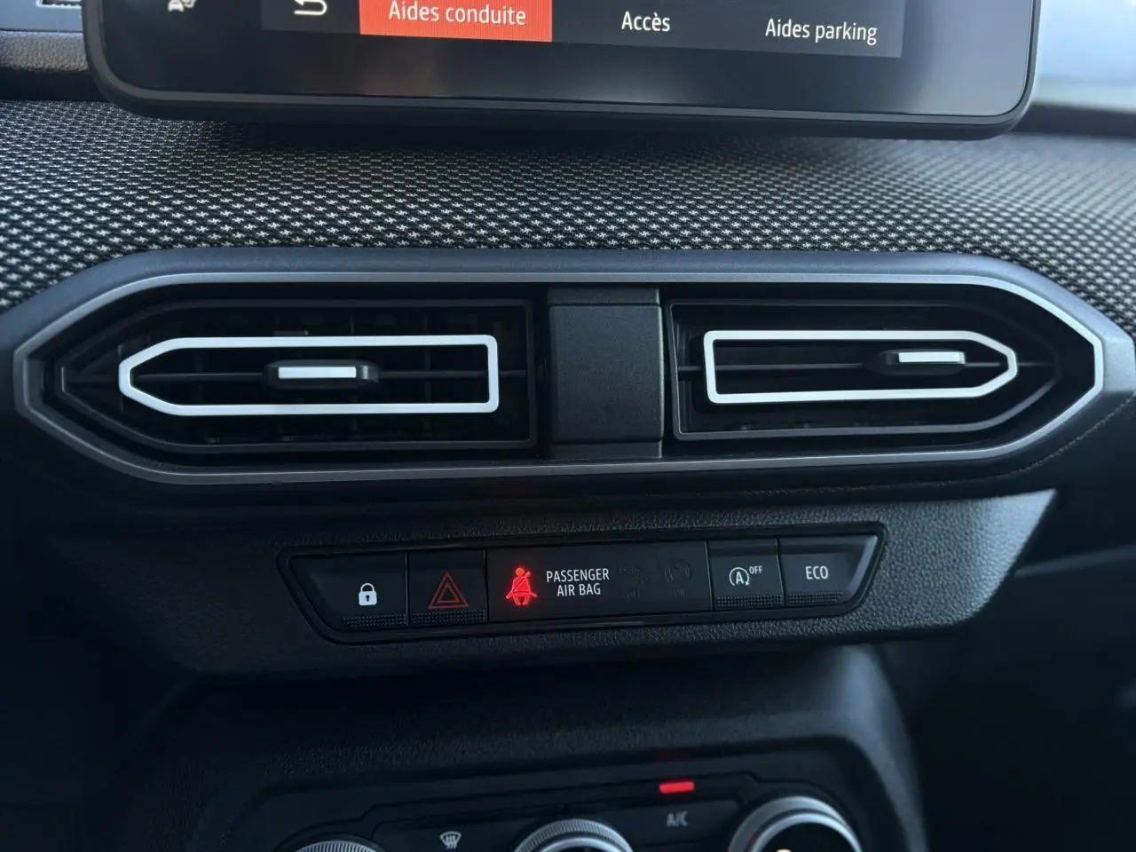 Vue rapprochée des aérateurs centraux et des boutons de contrôle du tableau de bord du Dacia Jogger gris Schiste 2025.