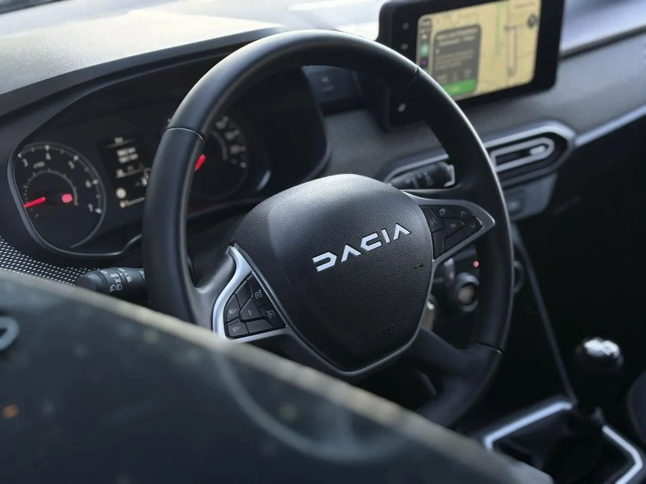 Vue rapprochée du volant noir du Dacia Jogger 2025 avec tableau de bord et écran tactile GPS en arrière-plan.