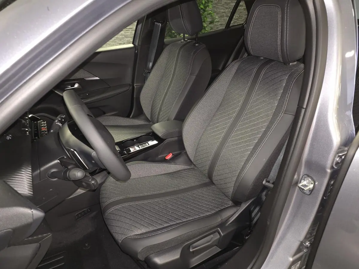 Vue intérieure côté conducteur de la Peugeot 2008 gris 2025, sièges tissu et TEP avec surpiqûres Quartz et volant cuir.