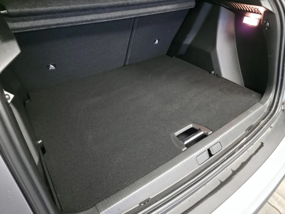 Coffre ouvert vu de l'arrière d'un Peugeot 2008 gris 2025, avec tapis noir et éclairage intérieur allumé.