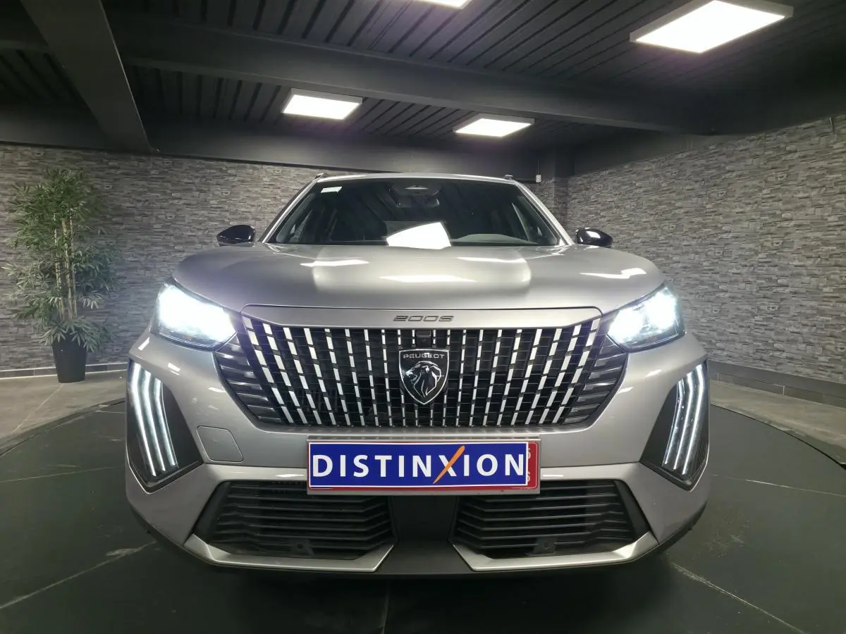 Vue avant du Peugeot 2008 gris 2025 avec calandre verticale chromée et feux LED allumés dans un showroom.