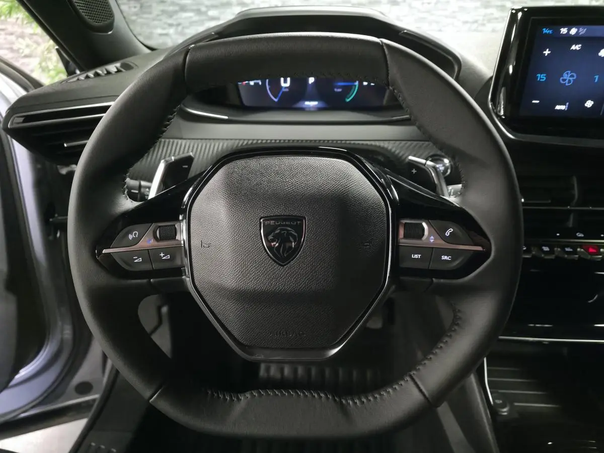 Vue rapprochée du volant compact noir de la Peugeot 2008 2025 avec commandes multimédia intégrées et tableau de bord numérique.