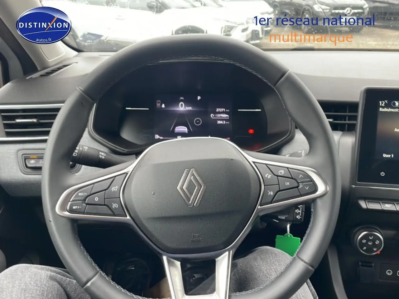 Vue intérieure centrée sur le volant multifonction noir d'une Renault Clio V blanche, avec tableau de bord digital et écran tactile visible.