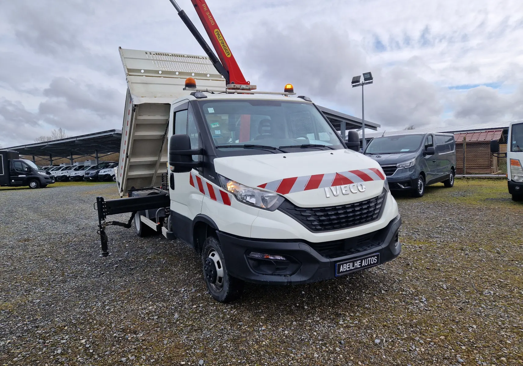 IVECO Daily Chassis Cabine blanc vu en 3/4 avant droit, benne relevée et grue Palfinger rouge déployée.