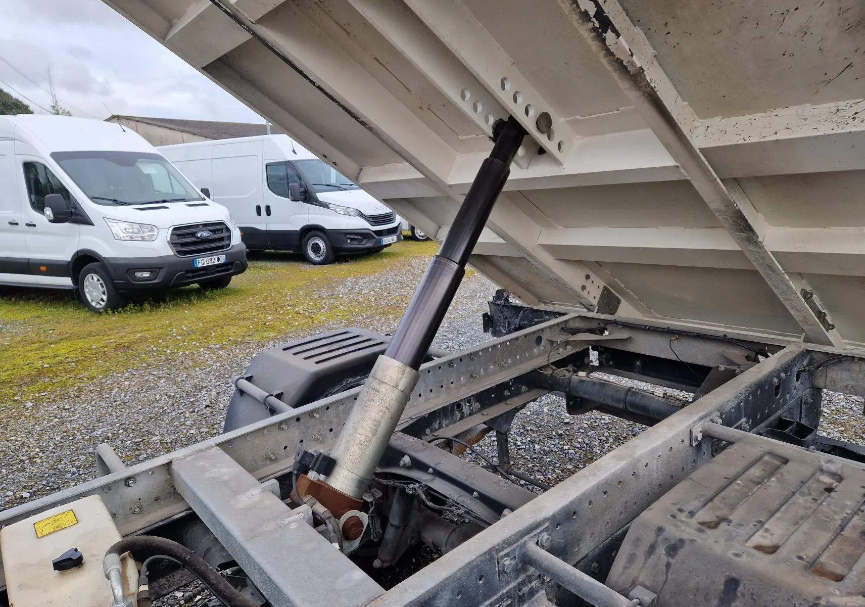 Vue rapprochée sous la benne relevée du camion blanc Iveco Daily 35C14 avec grue Palfinger et roues jumelées.