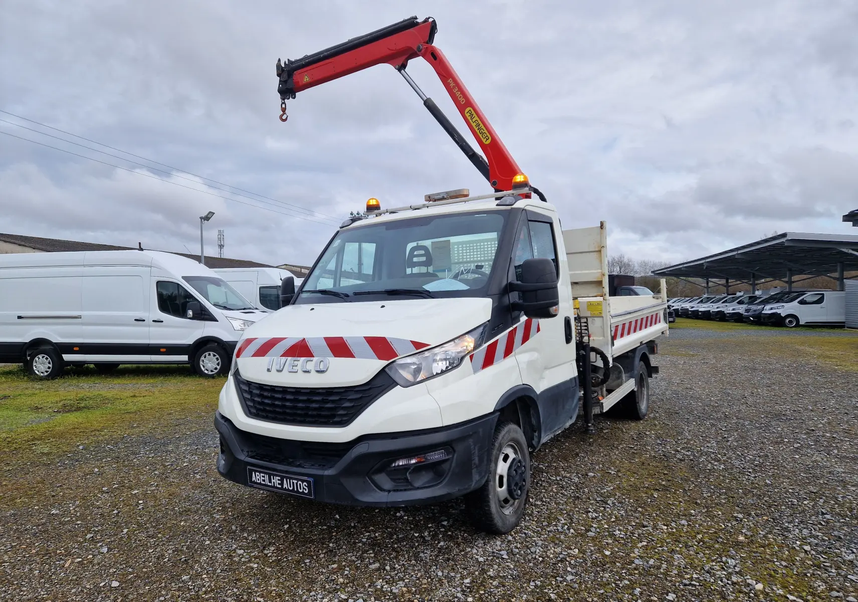 IVECO Daily Chassis Cabine blanc en 3/4 avant droit avec grue Palfinger rouge et benne arrière sur terrain gravillonné.