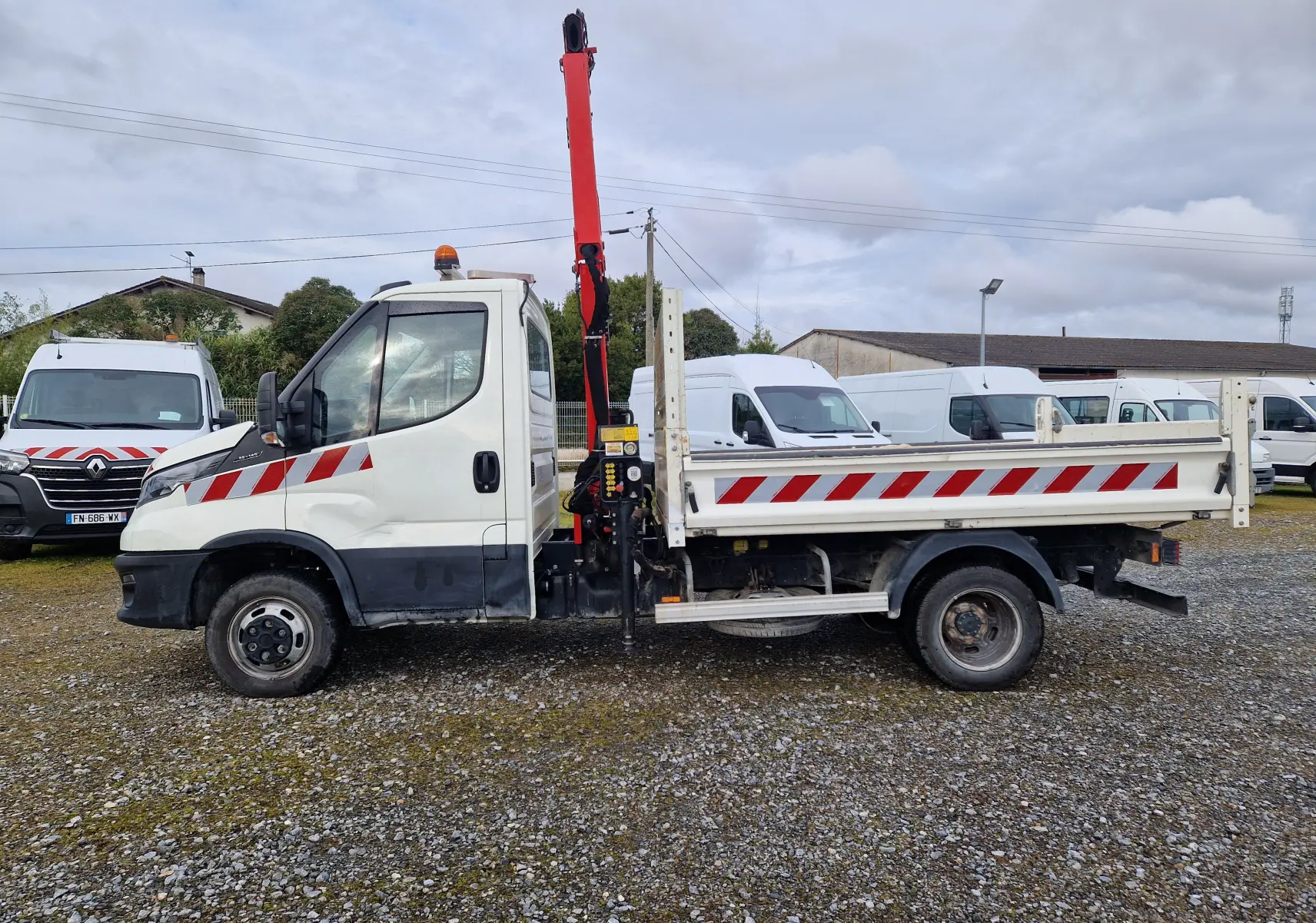 Vue de profil côté gauche d’un Iveco Daily blanc avec benne et grue rouge Palfinger, roues jumelées et bandes réfléchissantes rouges.