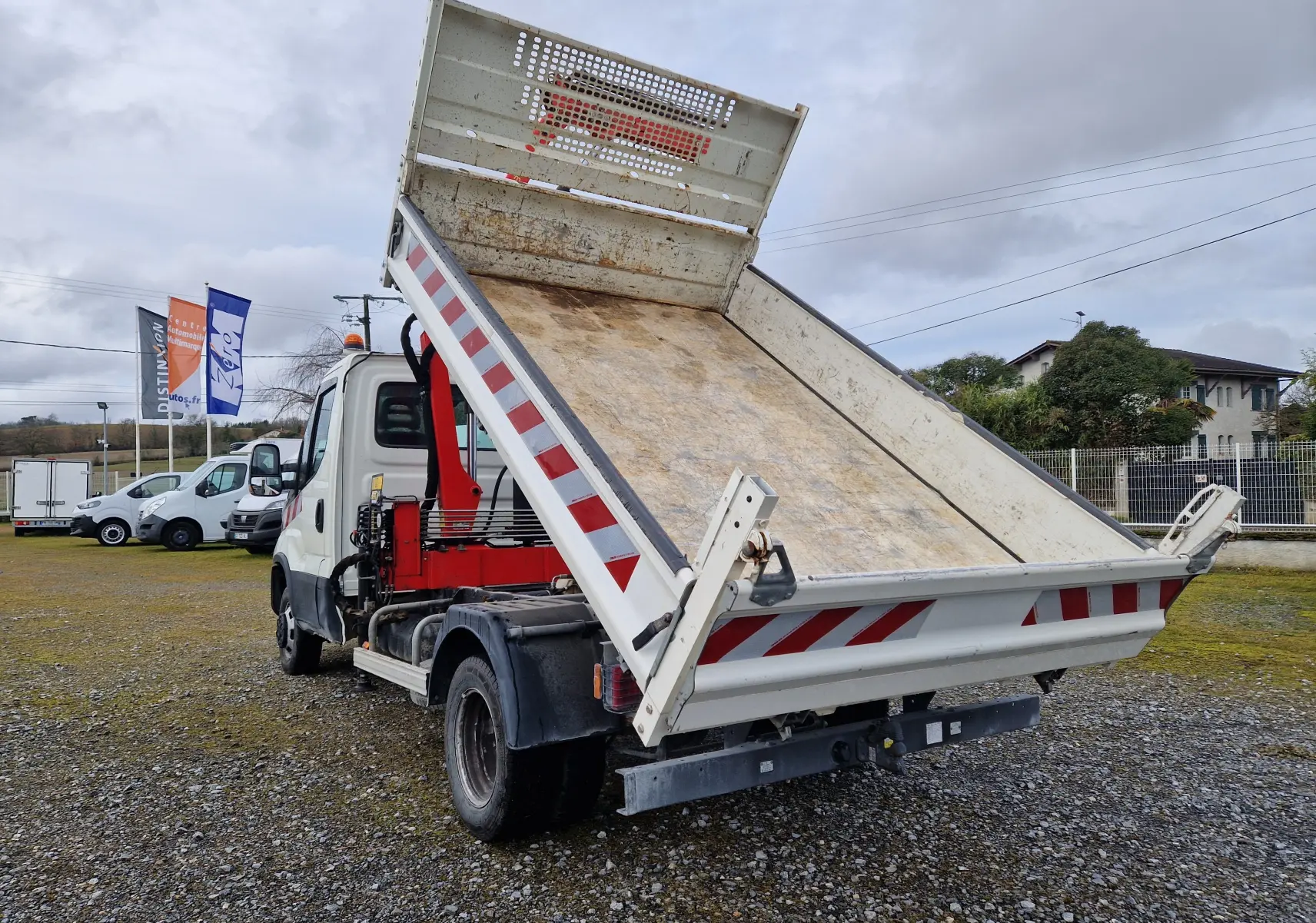 IVECO Daily Chassis Cabine blanc vu 3/4 arrière avec benne relevée et grue Palfinger rouge visible.