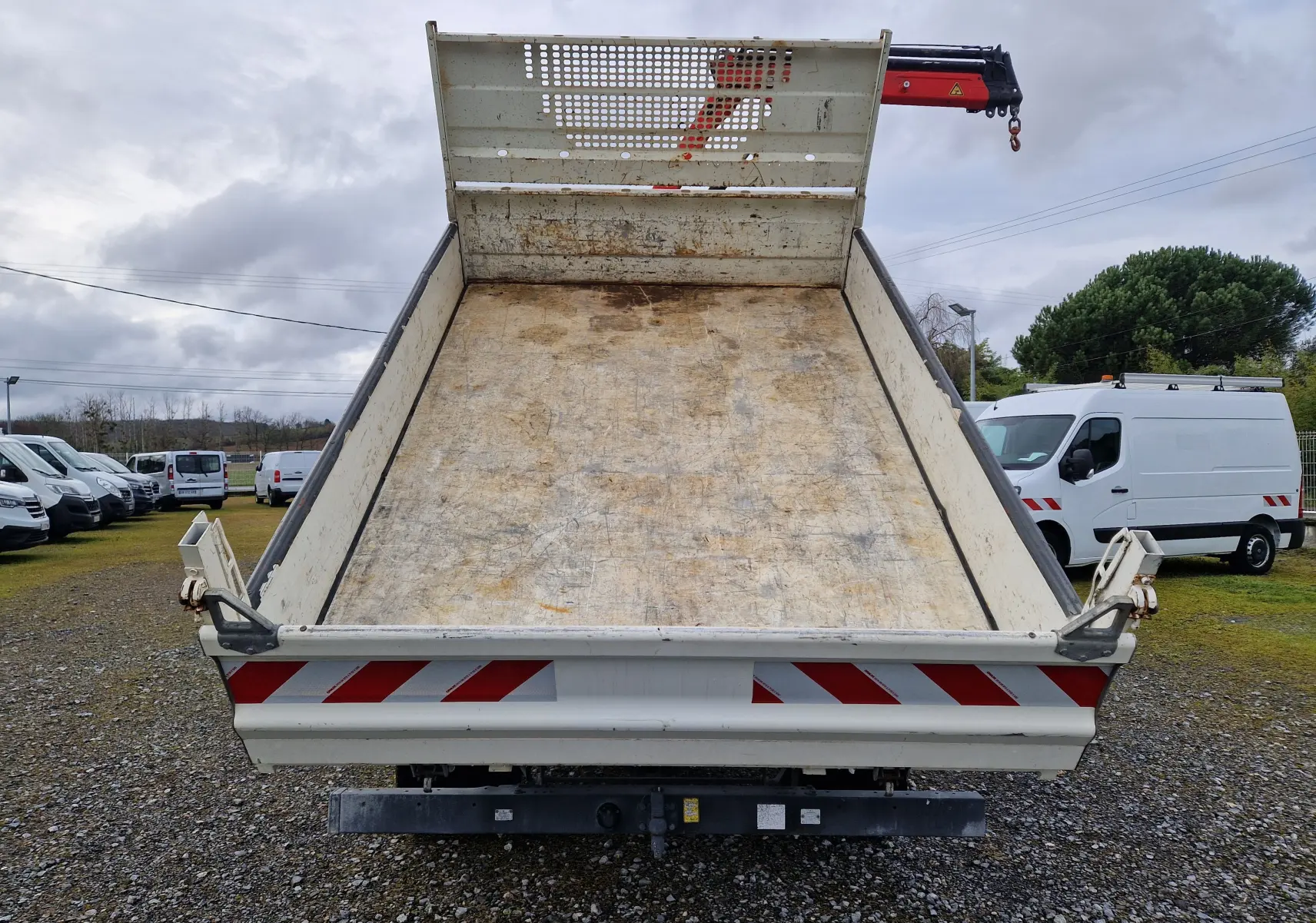 Vue arrière en contre-plongée de la benne blanche relevée d’un Iveco Daily Châssis Cabine avec grue Palfinger rouge.