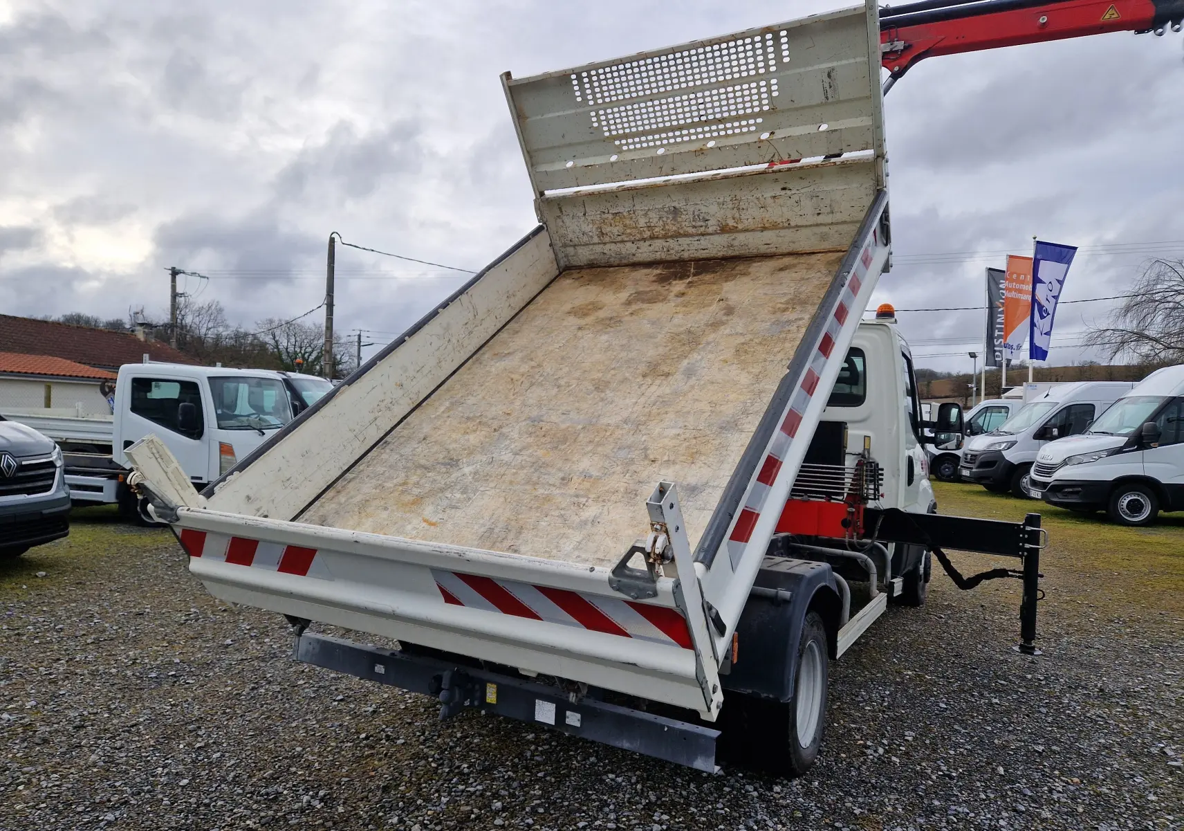 IVECO Daily Chassis Cabine blanc vu 3/4 arrière avec benne relevée et grue Palfinger déployée sur stabilisateur.