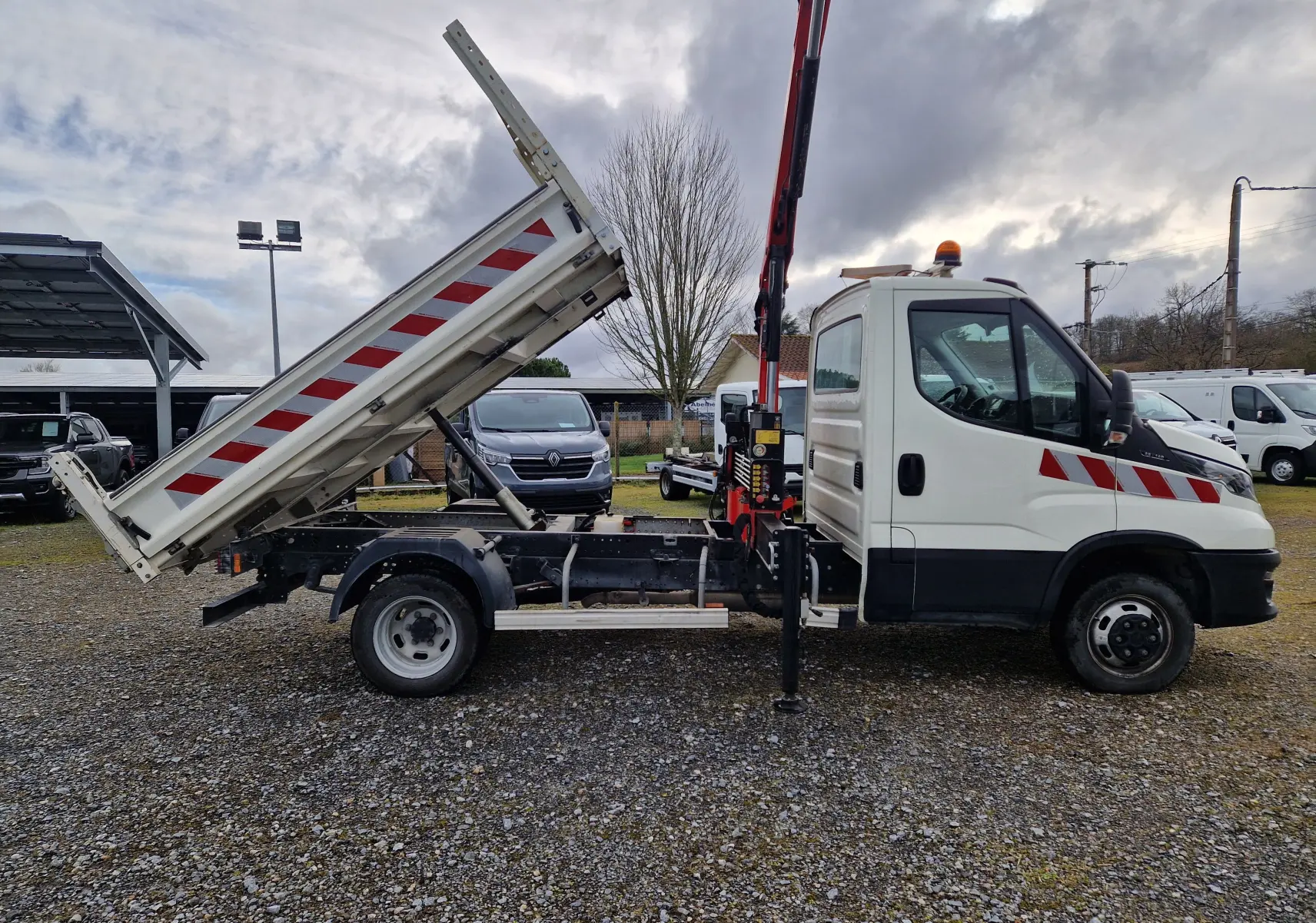 Vue de profil droit d’un Iveco Daily blanc 35C14 avec benne relevée et grue Palfinger rouge en position levée.