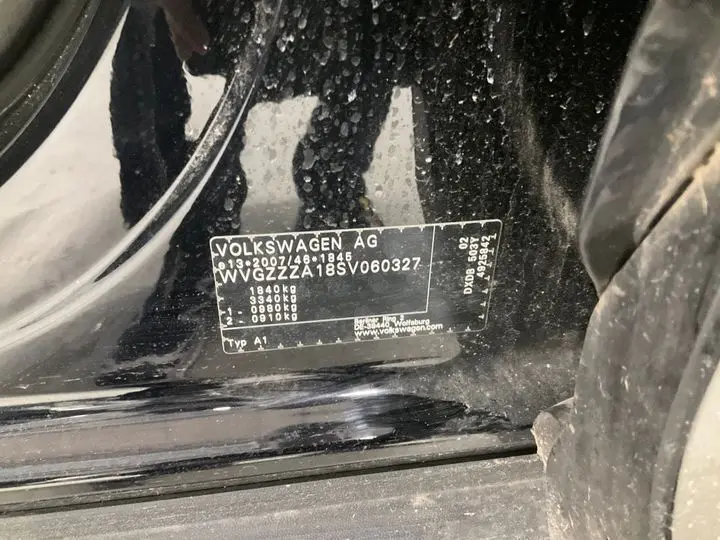 Gros plan sur l’étiquette constructeur noire du Volkswagen T-Roc noir intense, visible dans l’encadrement de porte côté gauche.