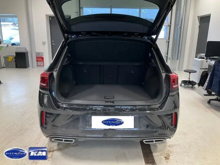 Vue arrière du Volkswagen T-Roc noir intense 2025 avec coffre ouvert, double sortie d'échappement et feux LED visibles.