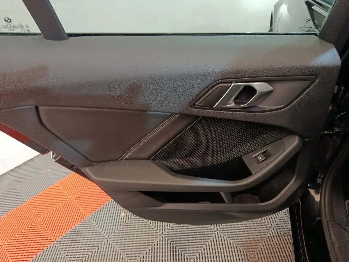 Vue intérieure du panneau de porte côté gauche noir de la BMW Série 1 118i Edition Sport 2023 avec poignée et commande de vitre.