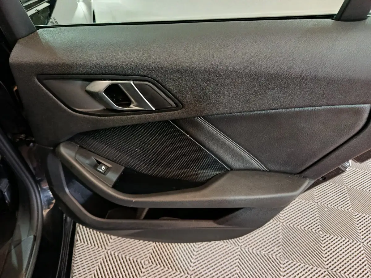 Gros plan sur la porte intérieure côté gauche noire de la BMW Série 1 118i Edition Sport avec poignée argentée et commande de vitre.