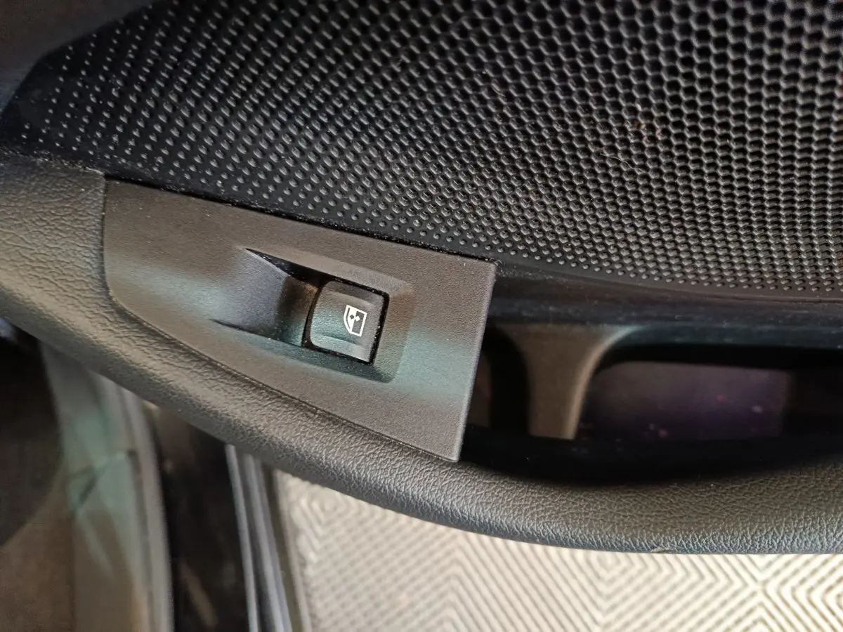 Gros plan sur le bouton de commande de lève-vitre côté conducteur dans l'habitacle noir de la BMW Série 1.