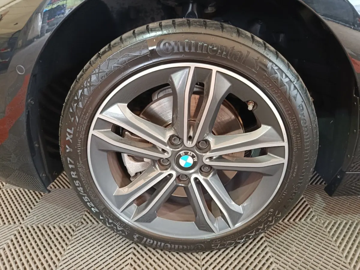 Gros plan sur la roue avant droite noire d'une BMW Série 1 118i Edition Sport avec jante alliage gris foncé.