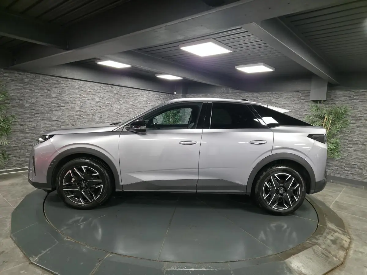 Vue de profil côté gauche d’un Peugeot 3008 gris métallisé 2025 avec jantes alliage noires et toit noir dans un showroom.