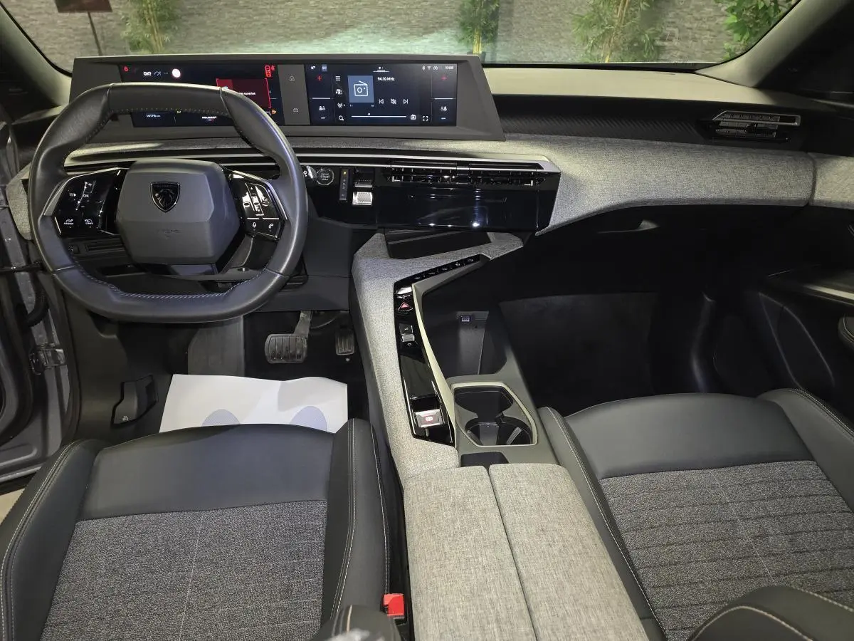 Intérieur avant du Peugeot 3008 gris 2025, tableau de bord avec double écran HD et sellerie tissu gris et cuir noir.