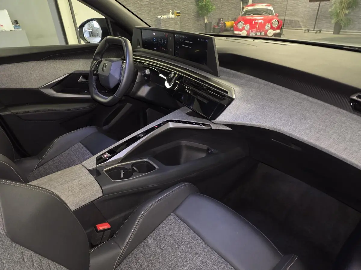 Intérieur de la Peugeot 3008 Hybrid 2025 vu côté passager, avec tableau de bord tissu gris et volant compact noir.