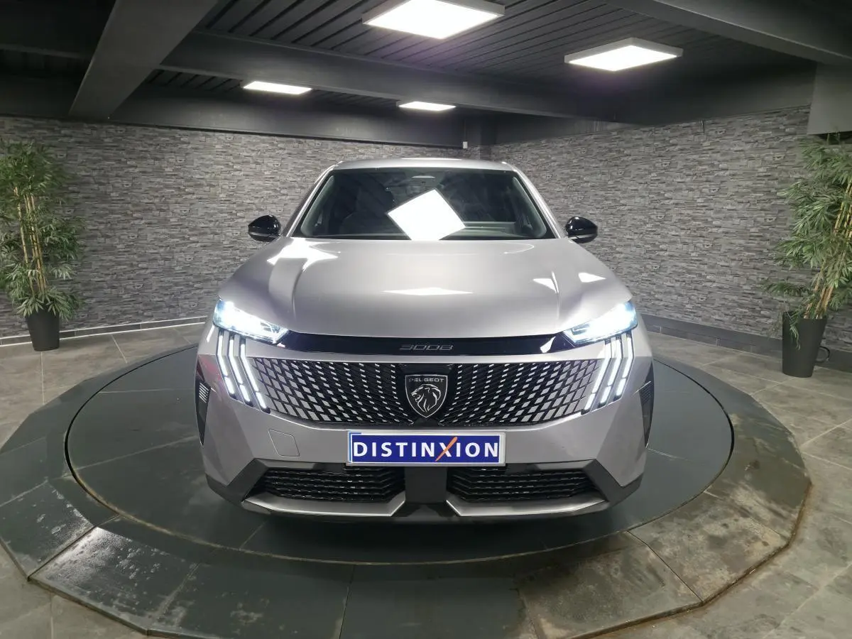 Peugeot 3008 gris vue de face, avec calandre noire laquée et feux LED allumés en intérieur showroom.