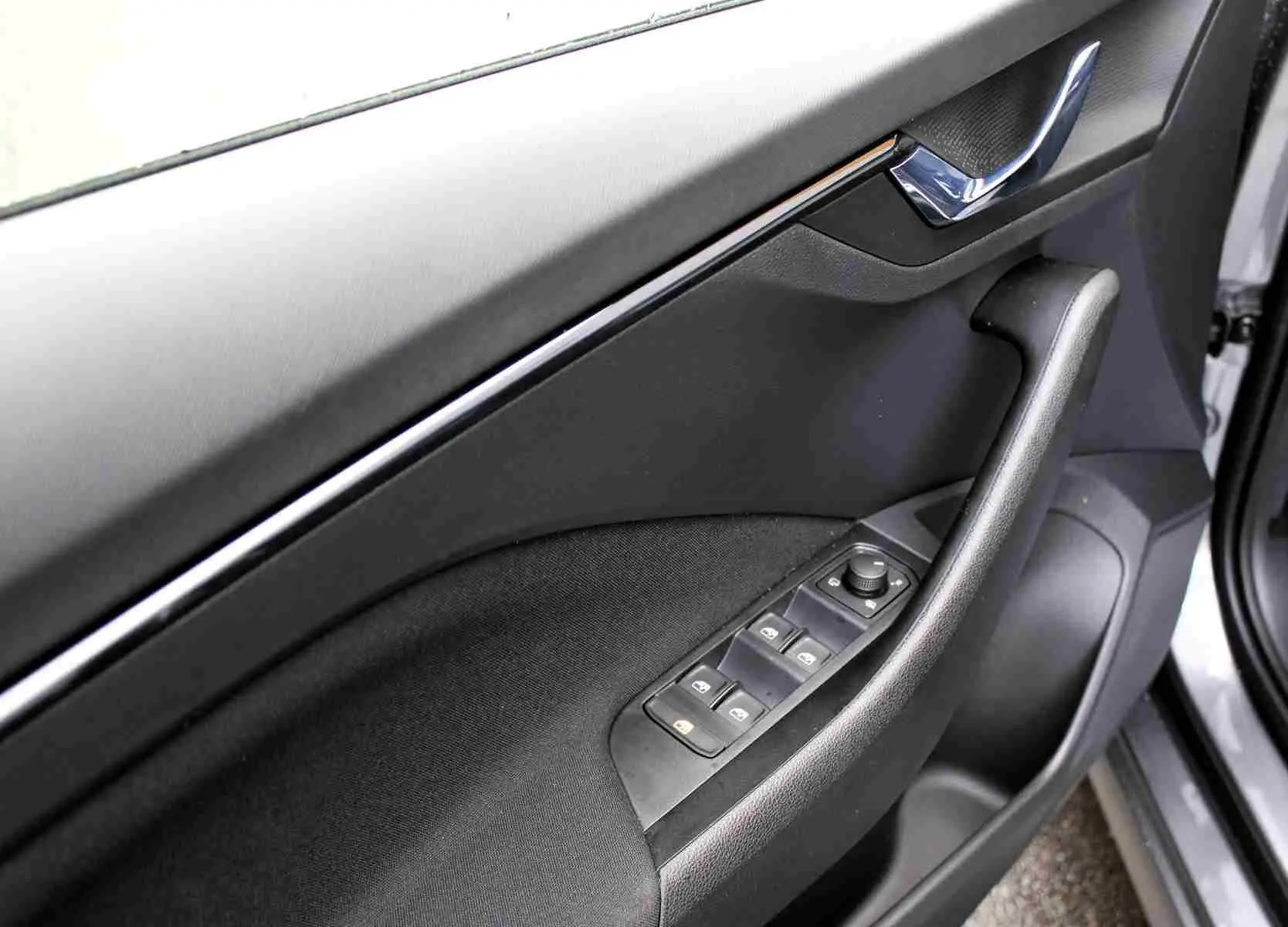 Gros plan sur la porte avant gauche du Skoda Kamiq gris graphite, montrant les commandes des vitres et la poignée intérieure chromée.