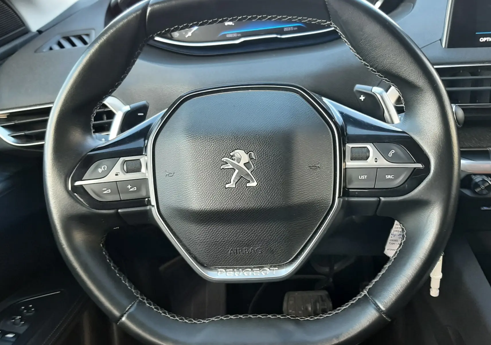 Vue rapprochée du volant noir du Peugeot 3008 2019, avec commandes intégrées et tableau de bord numérique en arrière-plan.