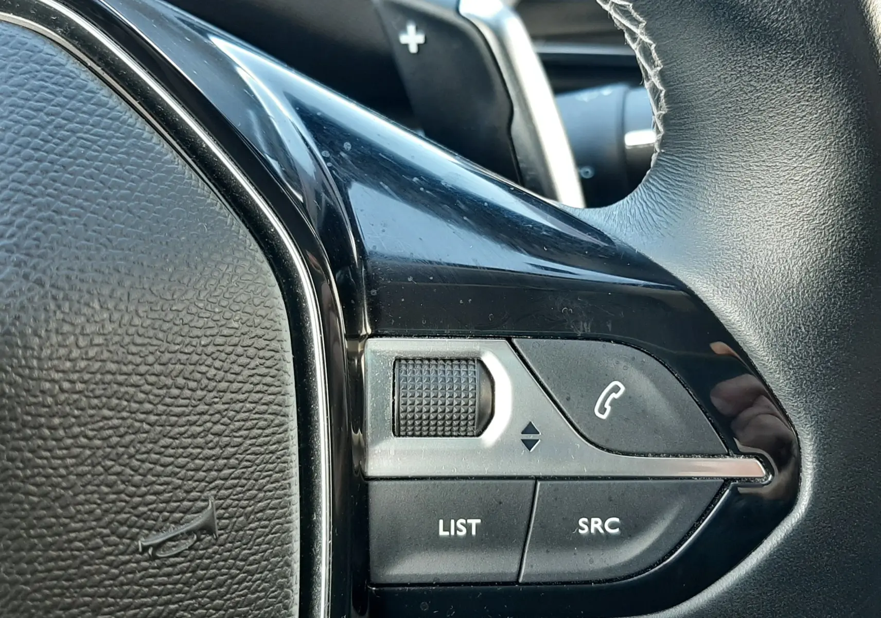 Gros plan sur les commandes gauche du volant noir du Peugeot 3008 gris Amazonite, avec molette et boutons d’appel.