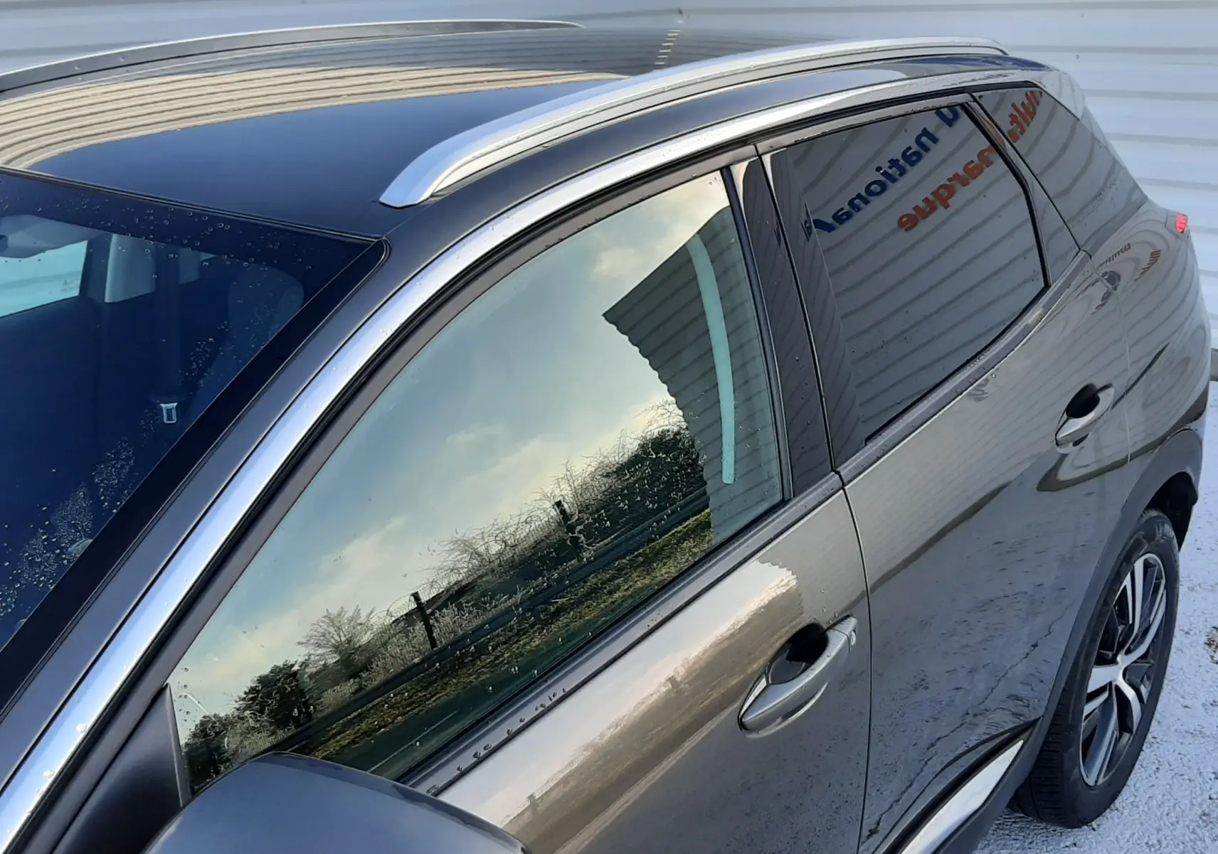 Vue latérale côté gauche du Peugeot 3008 gris amazonite 2019 avec barres de toit et vitres teintées.