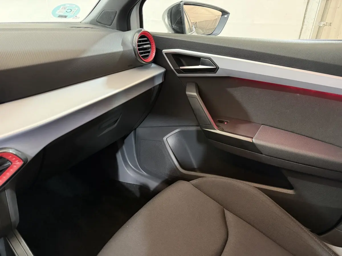 Intérieur SEAT Ibiza 2024 blanc, vue côté passager avant, tableau de bord gris avec aérateurs rouges.