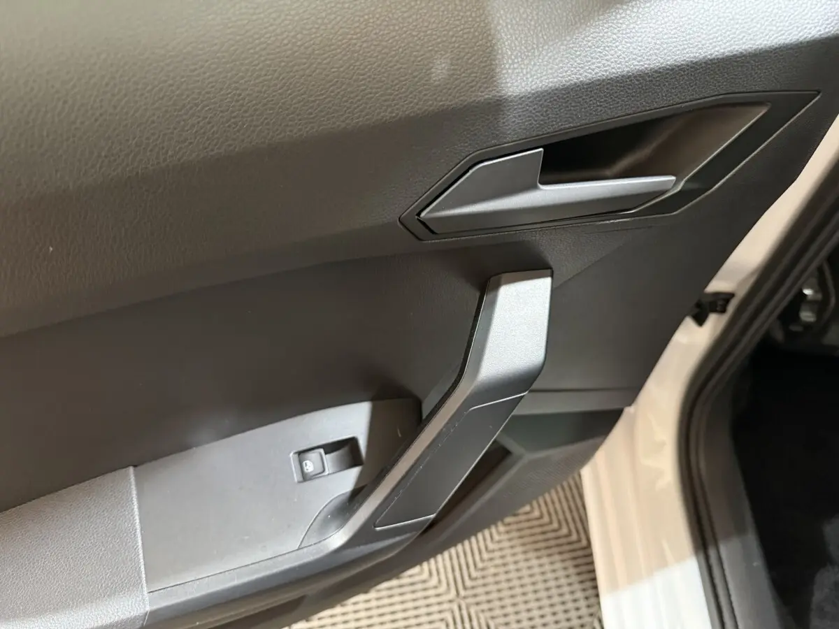 Gros plan sur la poignée intérieure côté conducteur de la SEAT Ibiza blanche, avec bouton de verrouillage des vitres.