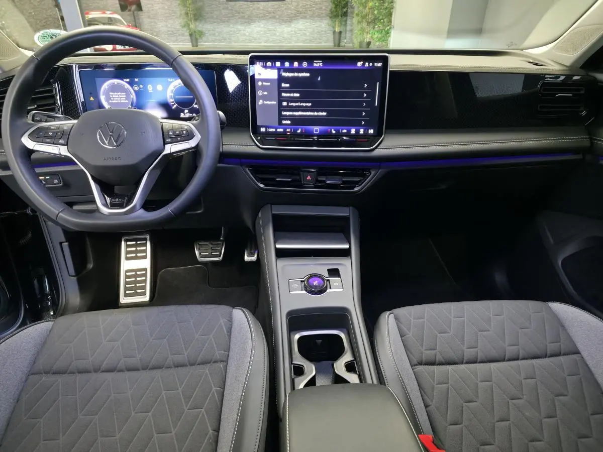 Vue intérieure avant du Volkswagen Tiguan 2025, tableau de bord noir avec écran tactile central et volant multifonction.