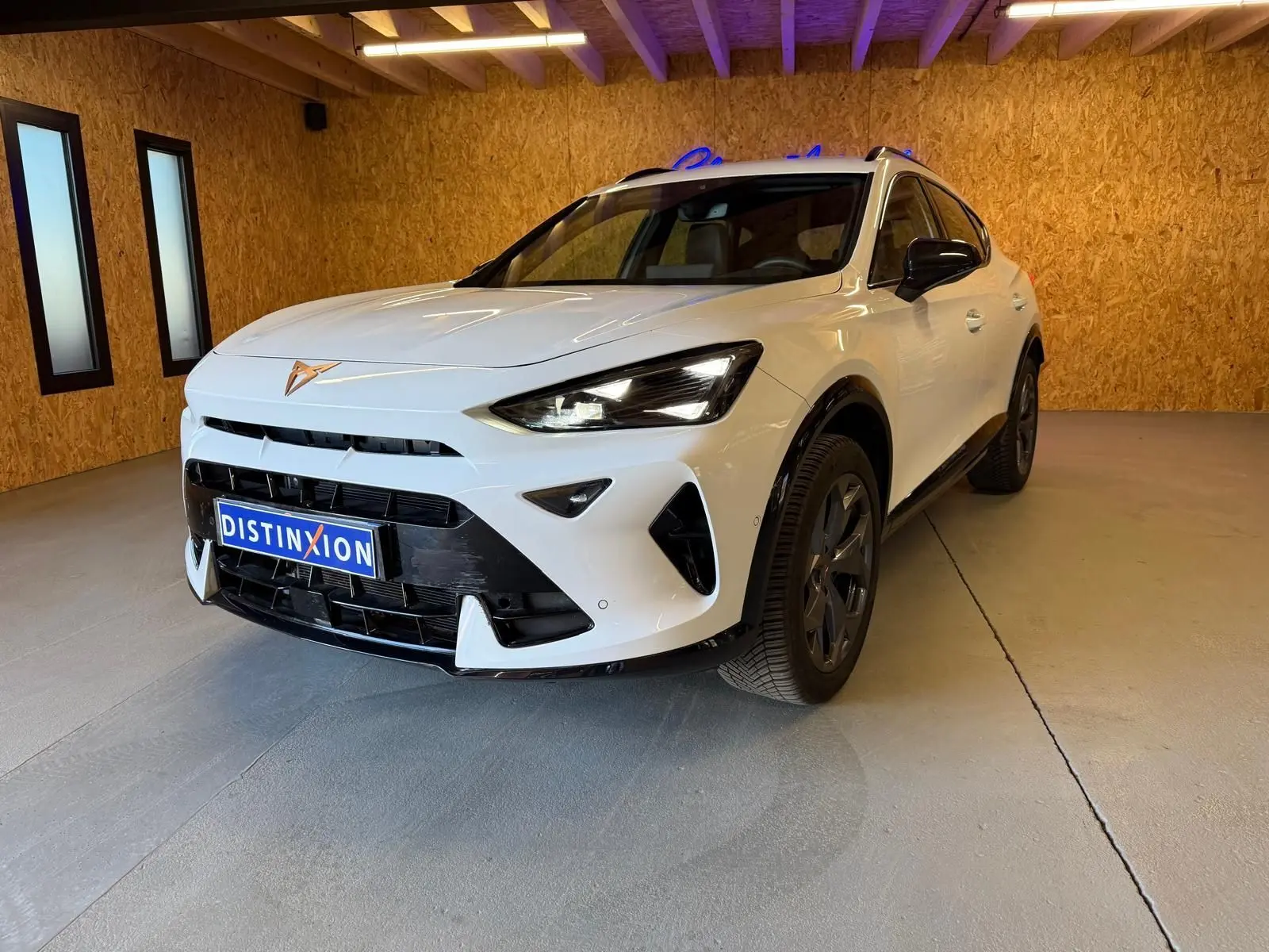 Vue 3/4 avant d'un CUPRA Formentor blanc avec détails noirs, calandre marquée et jantes foncées en intérieur bois.