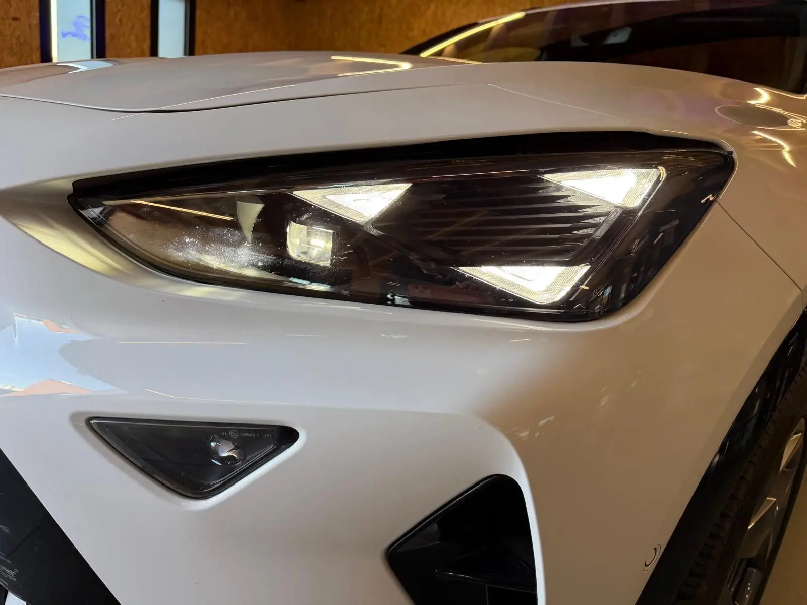 Gros plan sur le phare avant droit blanc du CUPRA Formentor 2.0 TDI 150 DSG7 V avec feux LED triangulaires allumés.