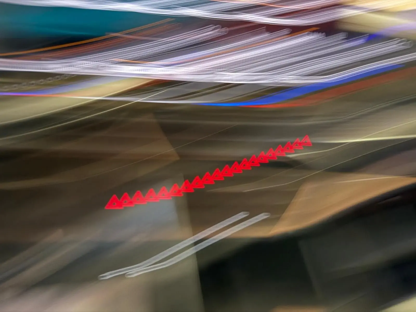 Image floue sans véhicule clairement visible, avec des lumières rouges et blanches étirées sur un fond sombre.