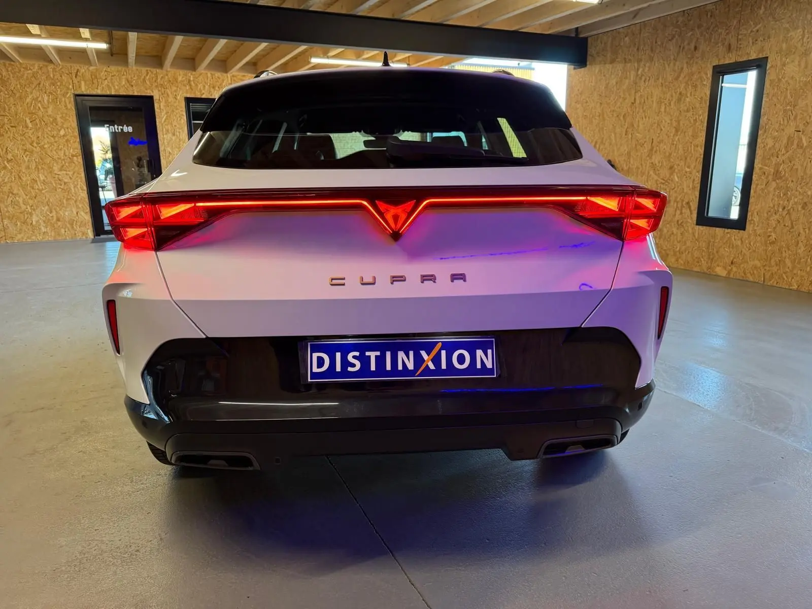 Vue arrière d'un CUPRA Formentor blanc 2025 avec feux LED allumés et logo lumineux dans un garage.