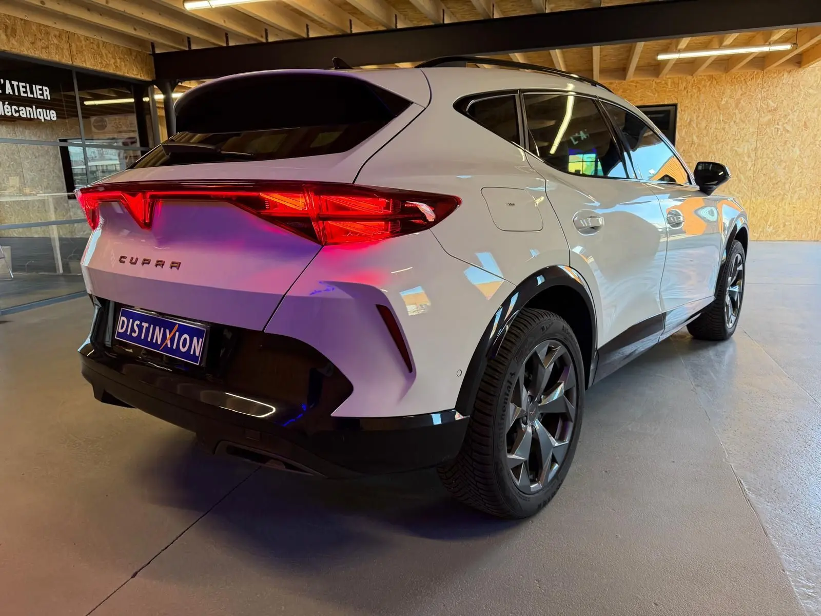 Vue 3/4 arrière droite du CUPRA Formentor blanc 2025 avec feux arrière LED et jantes foncées en intérieur d'atelier.