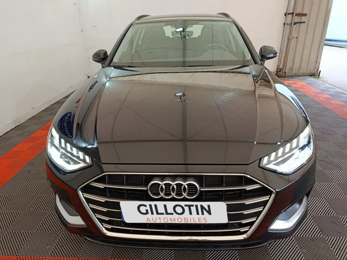 Vue avant d'une Audi A4 35 TFSI Business Line noire avec phares LED allumés dans un garage.