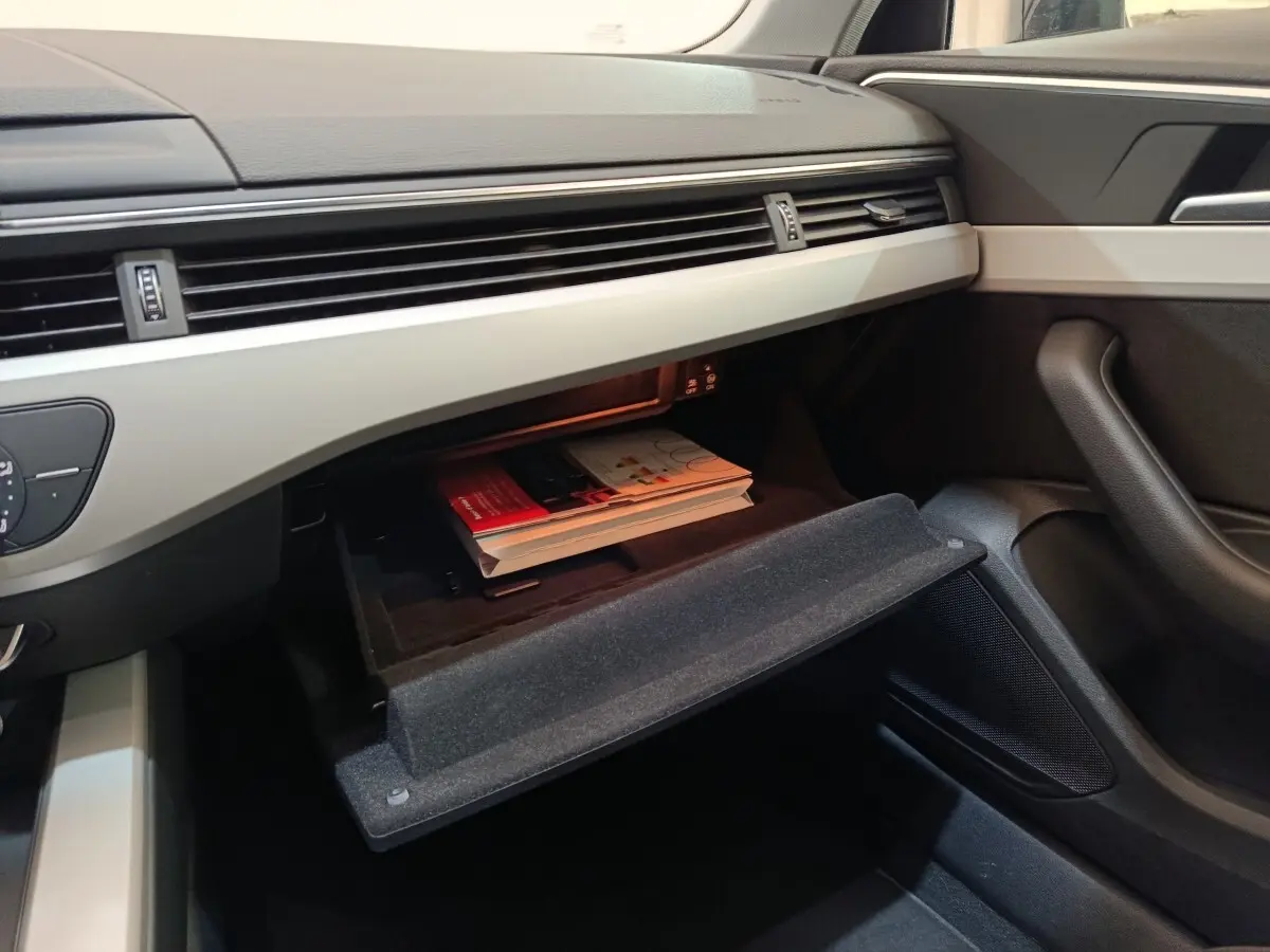 Vue intérieure côté passager de l'Audi A4 35 TFSI 2024, boîte à gants ouverte avec documents visibles.