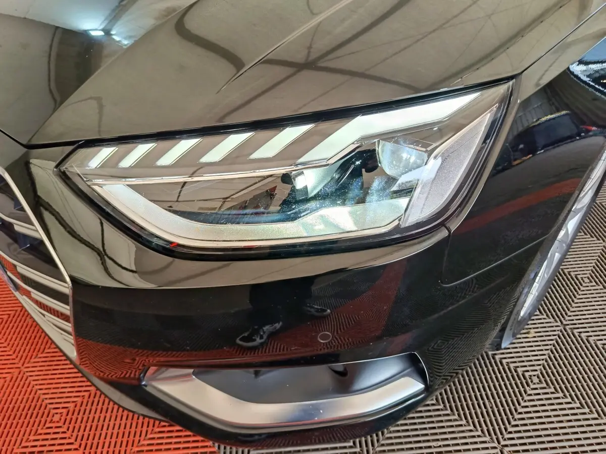 Gros plan sur le phare avant droit d'une Audi A4 35 TFSI noire, avec calandre et partie du pare-chocs visibles.