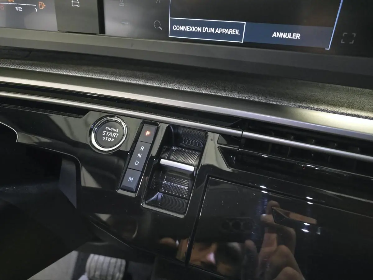 Gros plan sur la console centrale noire laquée du Peugeot 3008 Hybrid 2025 avec bouton start/stop et commande de boîte auto.
