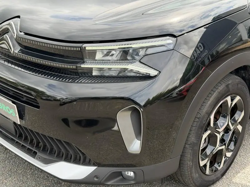 Gros plan sur l'avant droit noir Perla Nera du Citroën C5 Aircross 2024 avec phares LED et jante alu distinctive.