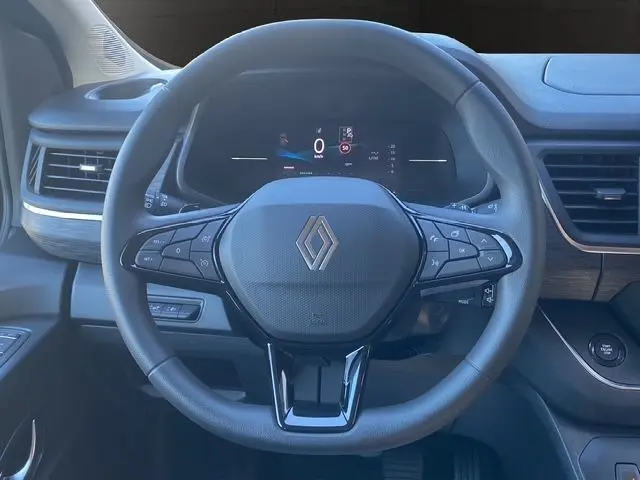 Volant noir Renault avec commandes intégrées, tableau de bord numérique et détails bois dans l'habitacle du Trafic Gris Urbain 2025.
