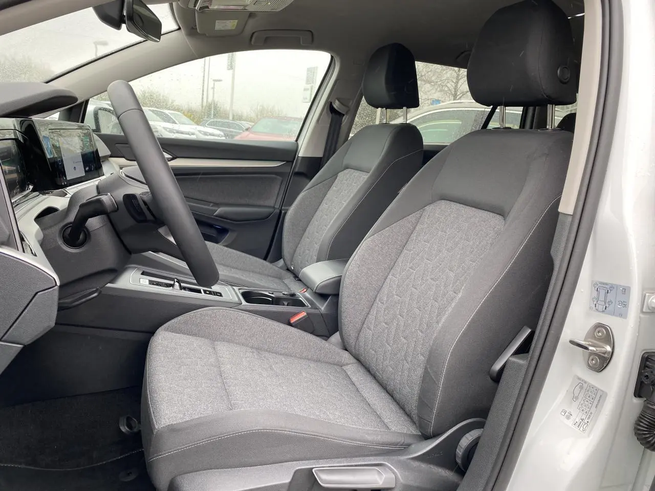 Vue intérieure côté conducteur de la Volkswagen Golf SW 2.0 TDI 116 DSG 7 Active Move avec sièges tissu gris et portière blanche ouverte.