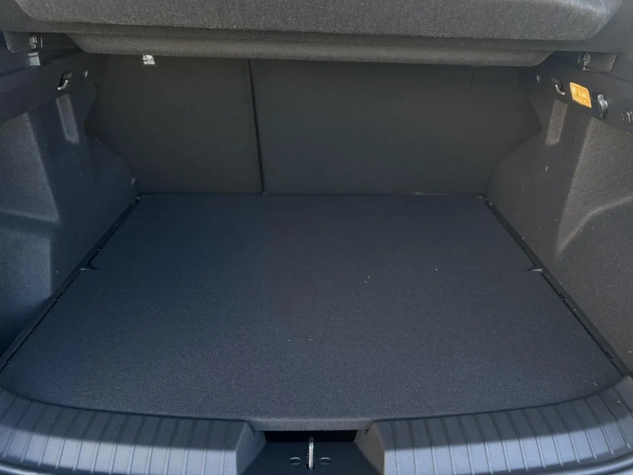 Coffre ouvert vu de face du Dacia Duster blanc Glacier, montrant un espace de chargement plat et spacieux.