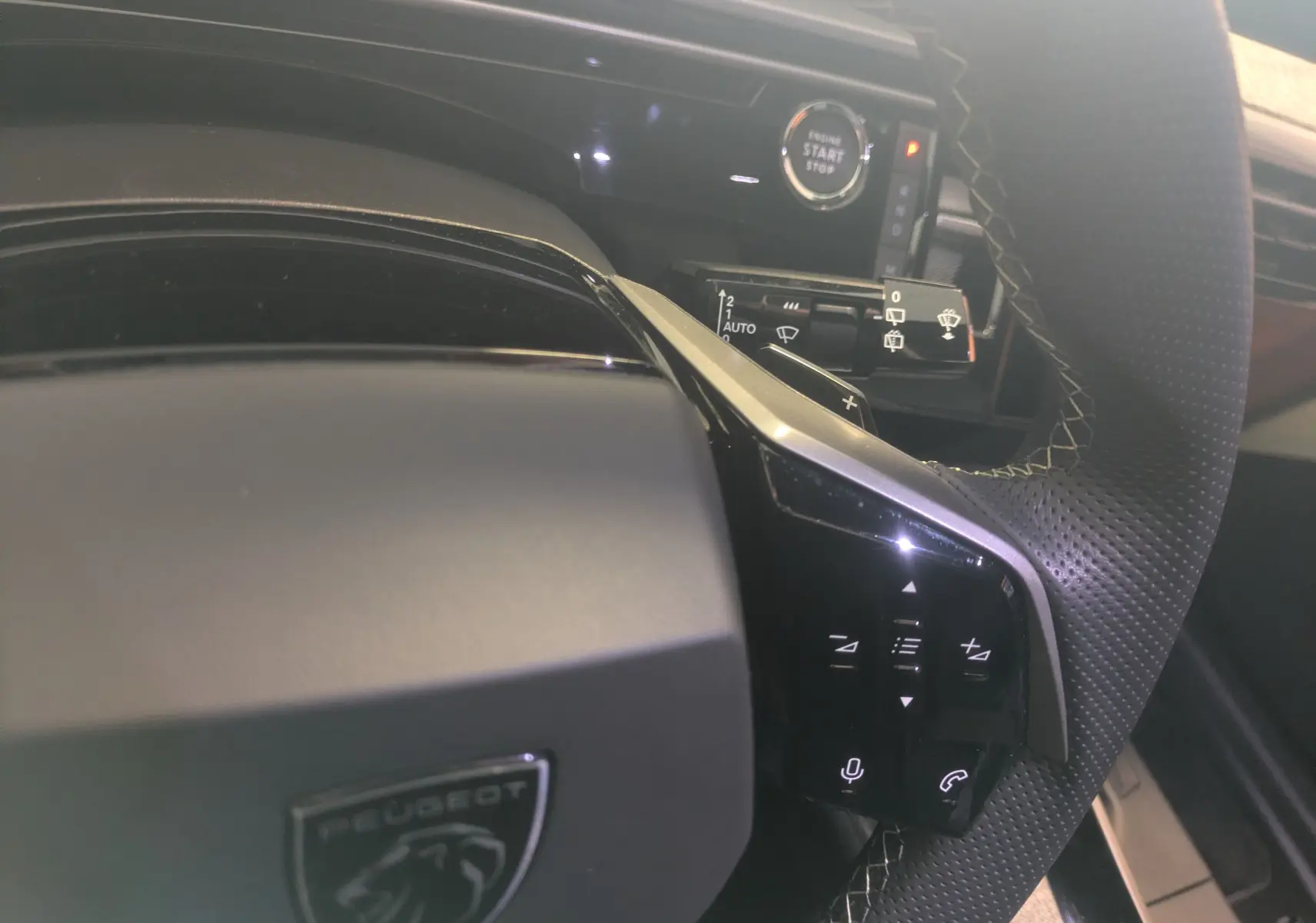 Gros plan sur le volant perforé et les commandes tactiles du Peugeot 5008 Hybride gris titane, avec bouton start/stop visible.