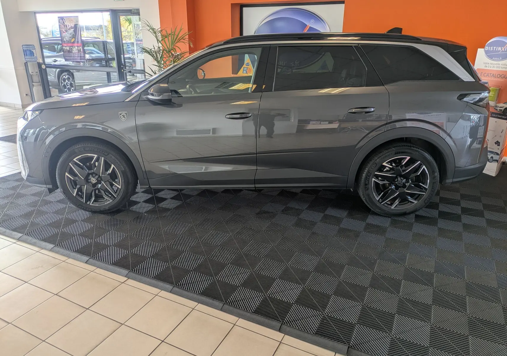 Peugeot 5008 hybride gris titane avec toit noir, vue profil côté gauche en intérieur showroom.