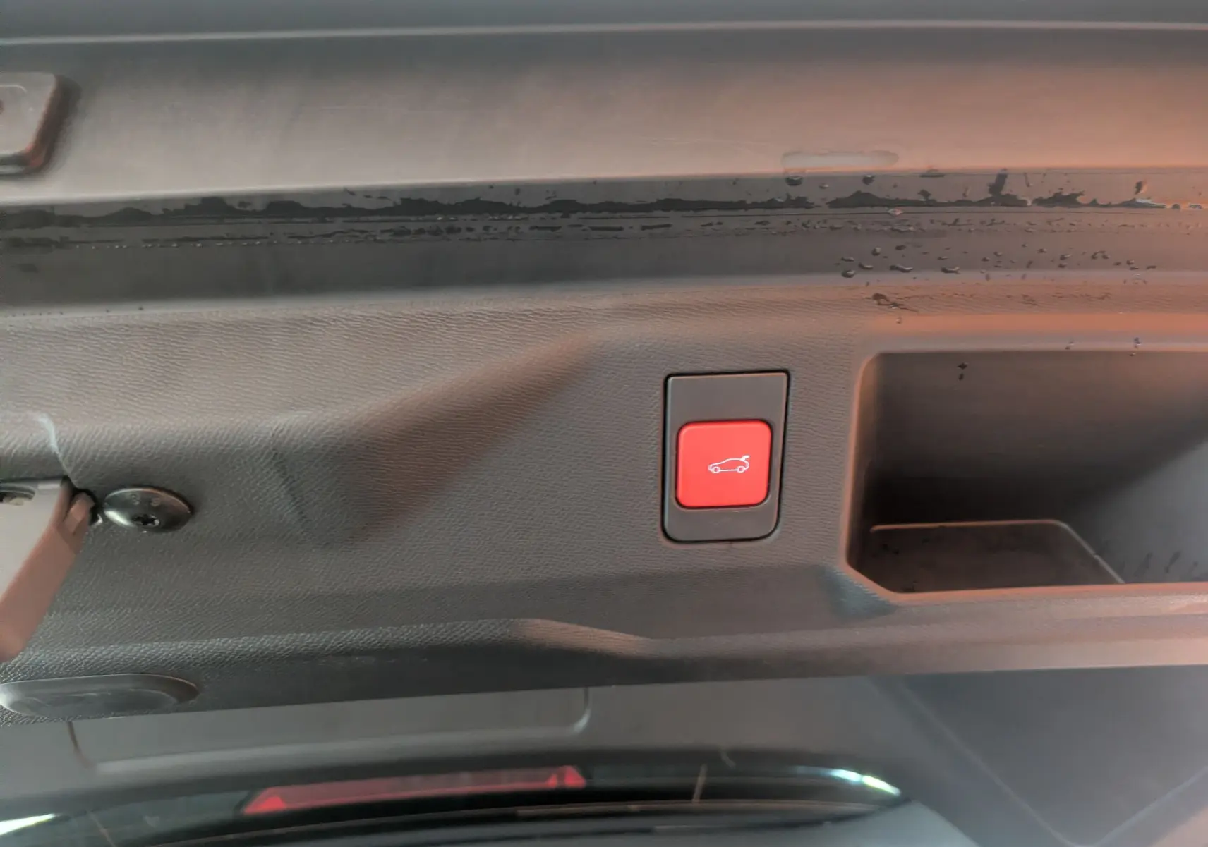 Bouton rouge d'ouverture électrique du hayon visible sur l'intérieur du coffre d'un Peugeot 5008 hybride gris titane.