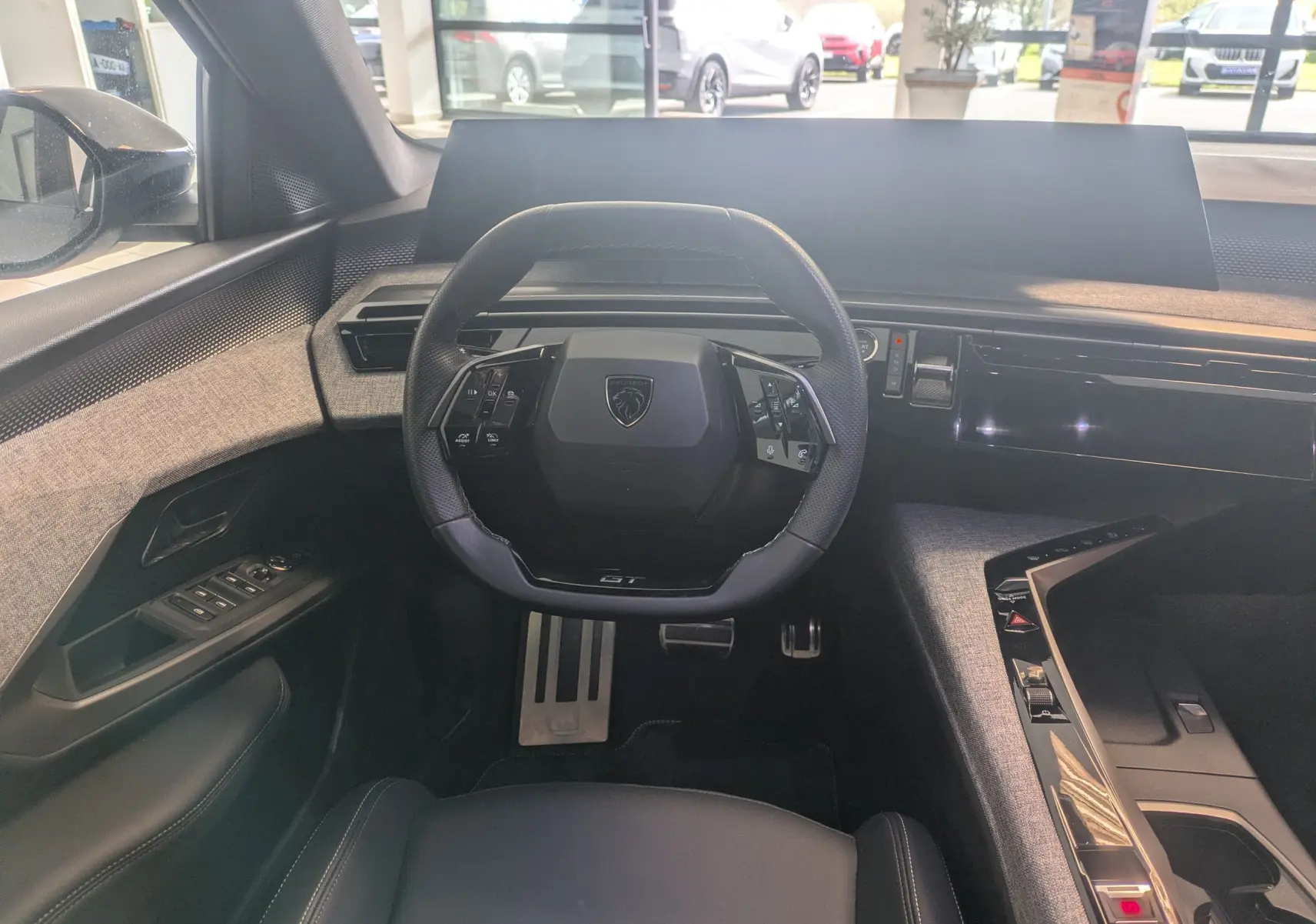 Vue intérieure frontale du poste de conduite du Peugeot 5008 hybride 2025, volant compact GT et tableau de bord numérique panoramique.