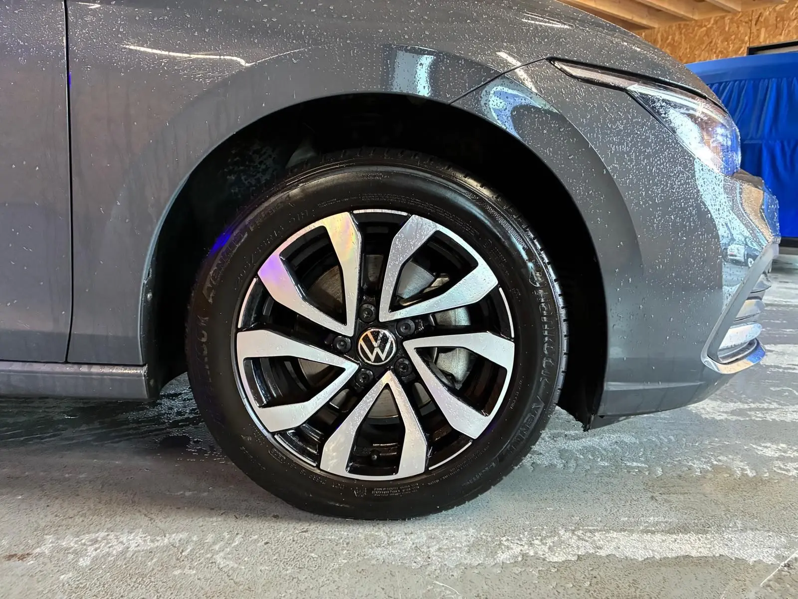 Gros plan sur la roue avant gauche d'une Volkswagen Golf gris 2022 avec jante alliage bicolore et carrosserie mouillée.